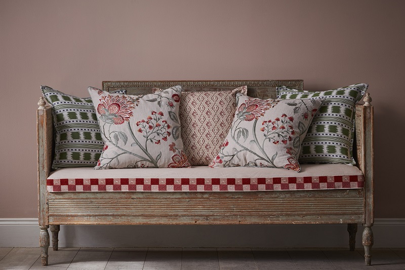 Banchetă tapițată cu bandă decorativă geometrică în tonuri de roșu și roz și perne decorative